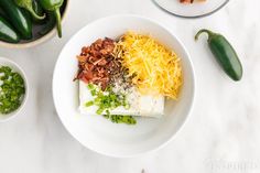 a bowl filled with different types of food on top of a white table next to green peppers