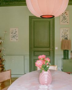 a pink vase sitting on top of a table next to a green door with flowers in it