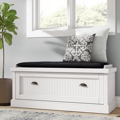 a white bench with black cushions and a plant in the window sill next to it