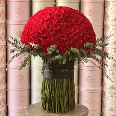 a large bouquet of red roses in a black vase on a table next to stacks of pink rolls