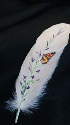 a white feather with a butterfly painted on it's side and some purple flowers