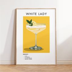 a white lady cocktail poster on a wall in a room with wood flooring and yellow walls