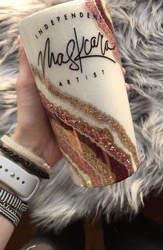 a person holding up a coffee cup with writing on the bottom and gold glitters