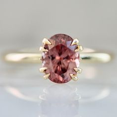 an oval shaped pink tourmaline stone sits on top of a gold band ring