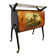 an antique wooden and metal magazine rack with paintings on the front, two shelves below it