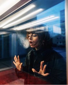 a woman standing in front of a window holding her hands out to the side and making a face