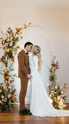 a bride and groom kissing in front of an arch decorated with floral arrangements for their wedding ceremony