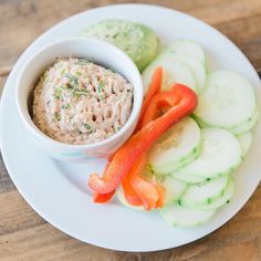 a white plate topped with cucumbers and carrots next to a bowl of dip