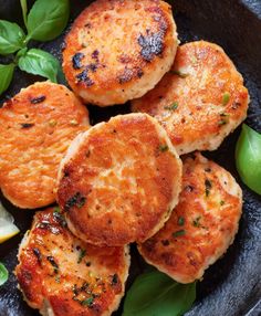 some crab cakes are on a plate with lemon wedges and basil leaves around them