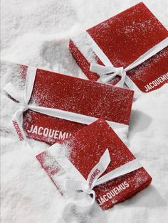 three red boxes covered in snow with white ribbon around the top and one is labeled jacquemini