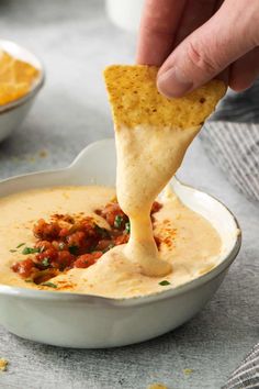 a person dipping tortilla chips into a bowl of dip with salsa in the background