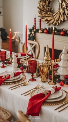 a table set for christmas dinner with red and gold place settings, candles and decorations