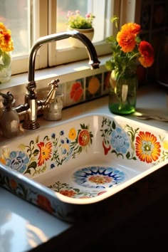 a sink with flowers painted on it in front of a window next to a faucet