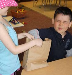 a young boy is holding a brown paper bag and looking at another child's face