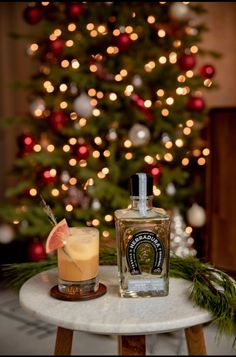 a christmas tree is in the background behind a bottle of booze and a drink on a small table