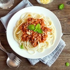 a white plate topped with spaghetti and sauce next to a glass of water on top of a wooden table