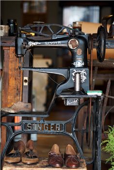 an old sewing machine sitting on top of a wooden table next to some shoes and plants