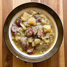 a bowl of soup with meat and potatoes on a wooden table next to a spoon