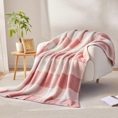 a pink and white blanket sitting on top of a couch next to a potted plant