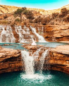 a man standing on top of a waterfall next to a body of water in front of a rocky cliff