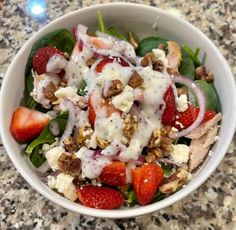 a salad with strawberries and dressing in a white bowl on a granite countertop