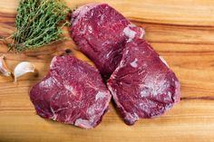 two pieces of raw meat sitting on top of a wooden cutting board