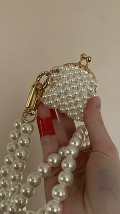 a hand holding a white beaded purse with pearls on the front and chain attached to it