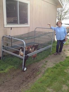 a woman standing next to a metal cage filled with chickens in front of a house