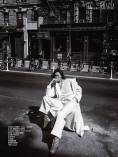 a woman sitting on the side of a road talking on a cell phone while wearing a white suit