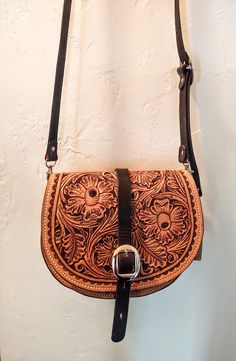 a brown and black purse hanging on a wall next to a white wall with a metal hook