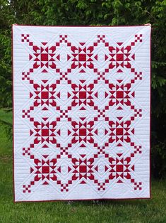 a red and white quilt on grass with trees in the background