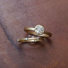 two gold rings with diamonds on them sitting next to each other in front of a brown background