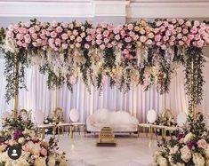 an elegant wedding setup with pink flowers and greenery on the wall, white couches and gold tables