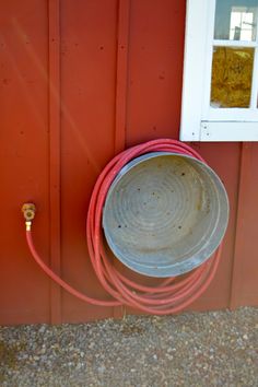 a bucket and hose attached to the side of a red building next to a window