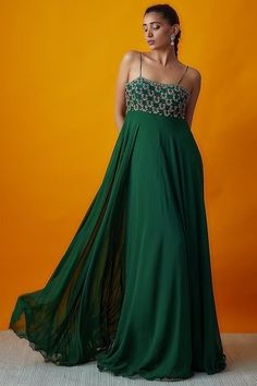 a woman in a long green dress poses for the camera with an orange wall behind her