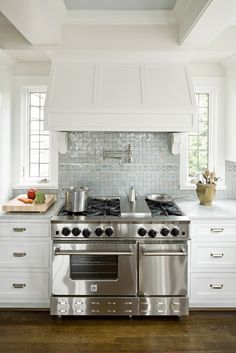 a stove top oven sitting inside of a kitchen next to a wooden floor and white cabinets