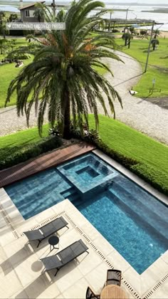 an aerial view of a swimming pool with lounge chairs and palm tree in the foreground