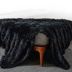 a black blanket on top of a bed next to a wooden footstool and chair