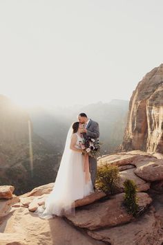 a bride and groom standing on top of a mountain