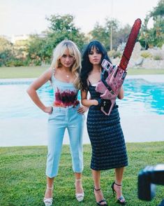 two women standing next to each other in front of a pool holding a chainsaw