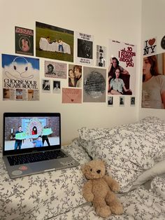 a laptop computer sitting on top of a bed next to a teddy bear and posters