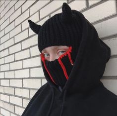 a person wearing a black and red knitted hoodie with horns on it's face