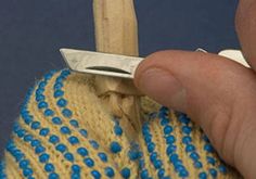 a hand holding a pair of scissors over a knitted sweater with blue dots on it