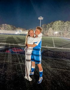 two people hugging each other in front of a soccer field at night with the lights on