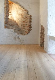 an empty room with wooden floors and brick walls in the corner that has a light coming from it