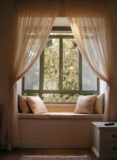 a window seat with two pillows on it in front of a curtained window sill