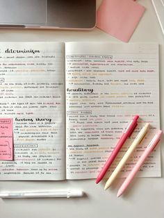 an open book with writing on it next to two pencils and a laptop computer