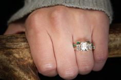 a person's hand with a ring on top of it and a tree branch in the background