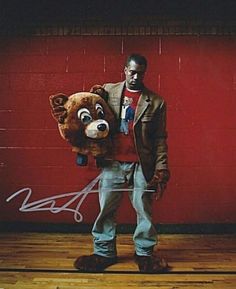 a man holding a large stuffed bear in front of a red brick wall and wooden floor