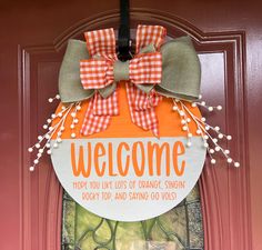 an orange and white welcome sign hanging on the front door to a house with pumpkins